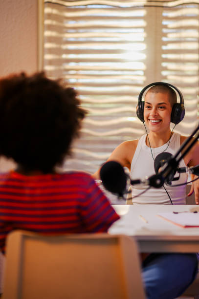 The cheerful interracial podcasters are sitting in a small home broadcasting studio
