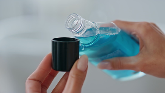 Woman hands pouring mouthwash in cap indoors close up. Unknown lady holding blue antibacterial liquid at bathroom. Unrecognizable girl using refreshing dental rinse. Morning care in bath room concept