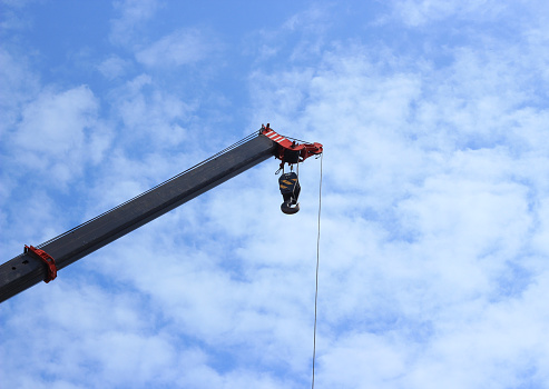 Iron beams hanging in the air, attached to a construction crane with chains, with a clear blue sky in the background.