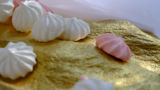 Closeup of sweet  twisted meringue cookies, white and pink colored. Golden stone podium. Sweet food, candy. Pastel