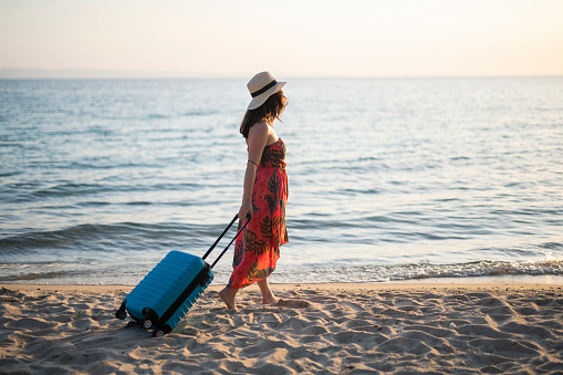 Young female traveller on seaside vacation with suitcase on the beach.