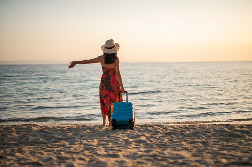 Happy young woman with suitcase on a beach holiday.