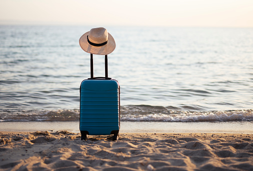 Suitcase with a sunhat on the beach.Seaside vacation consept.