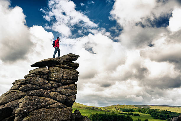 Hiker on top of a Rock A hiker standing on top of a large rock at Hound Tor in Dartmoor England overlooking a valley. outcrop stock pictures, royalty-free photos & images