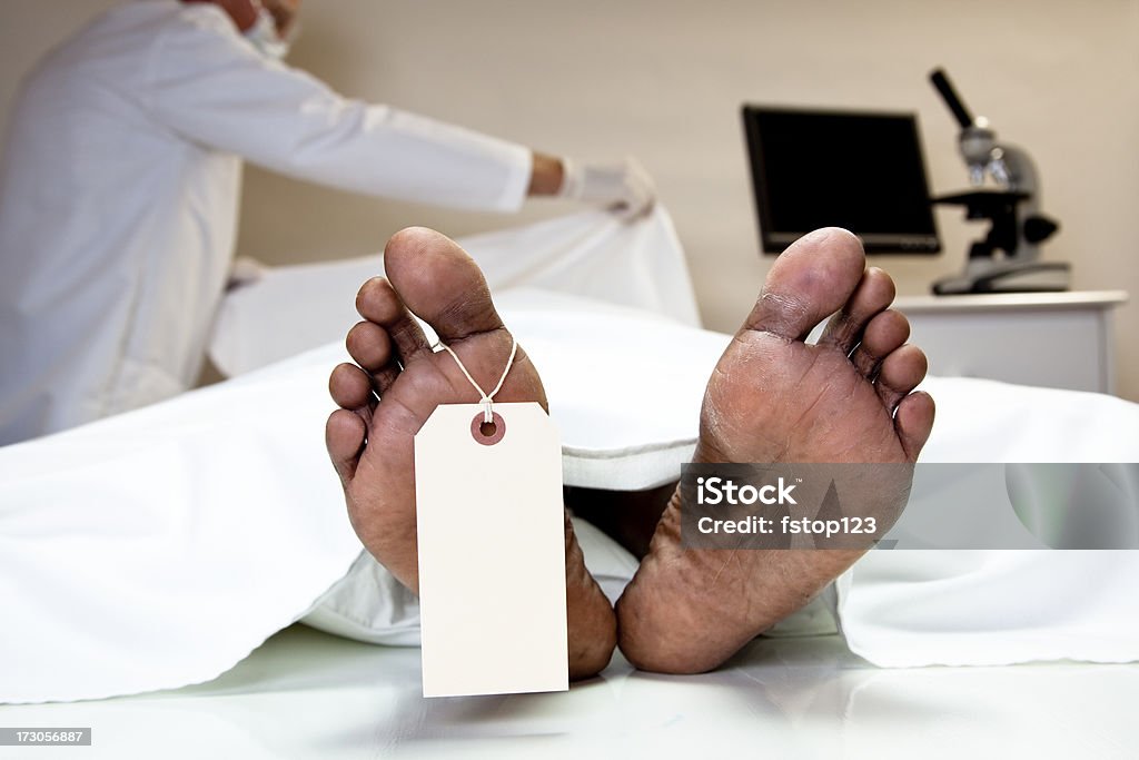 Mortician, coroner covering dead body in morgue. Feet, toe tag. Mortician, medical examiner covering dead body in morgue Death Stock Photo