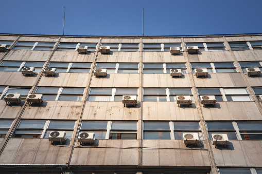 Picture of AC units on display on the facade of a decaying business building of the city center of Belgrade, Serbia, Europe, with cables falling down. Air Conditioning, as well as HVAC systems are considered to be consuming a lot of energy