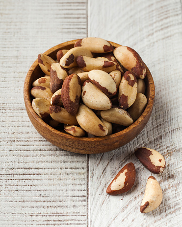 Dried Brazil nuts in a wooden plate on a white wooden background. The concept of nuts, healthy eating.