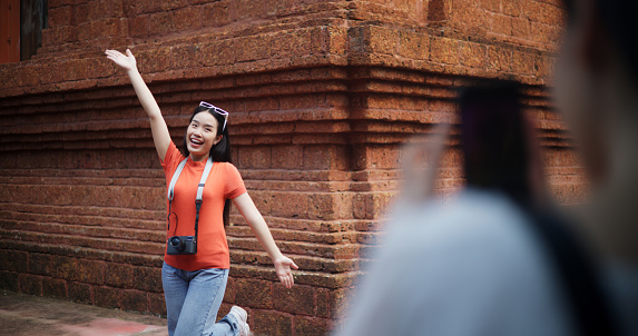 Portrait of Asian young female tourist taking a photo for a friend while visiting an ancient temple. Capture happy holiday moments through travel photos, people, and lifestyle concepts.