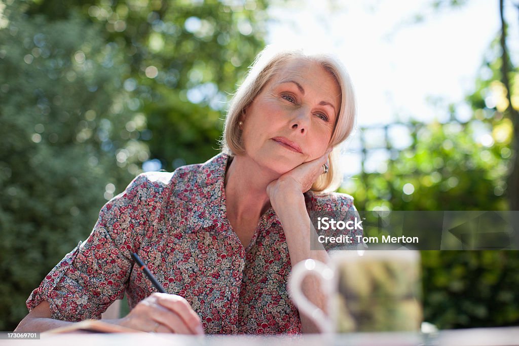 Pensif femme écrire dans cahier sur table du patio - Photo de 60-64 ans libre de droits