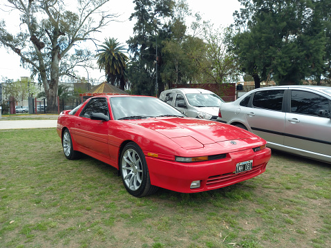 Lanús, Argentina - Sept 24, 2023: Old red 1990s sport Toyota Supra TRD coupe on the lawn at a classic car show in a park. Nature, trees