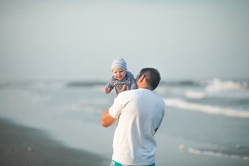 Happy Fathers day. Father and baby play on the beach. Dad and him Child together enjoying sunset. Loving single father hugs cute little son.