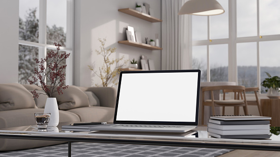 Home workspace with a white-screen laptop mockup, books, a coffee cup, and a flower vase on a modern coffee table in a modern, cosy living room. 3d render, 3d illustration