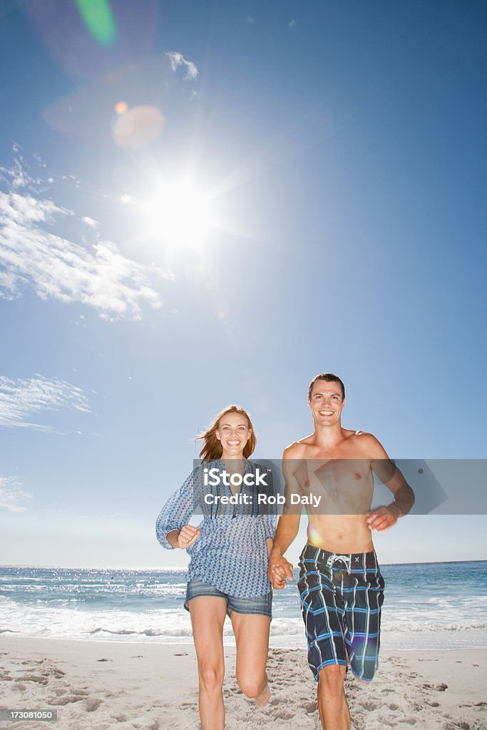 Sonriente Pareja corriendo en la playa y agarrar de la mano - Foto de stock de 20-24 años libre de derechos