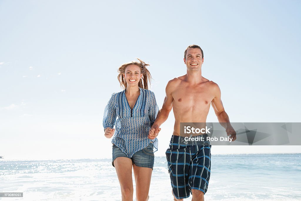 Souriant couple courir sur la plage, tenant les mains - Photo de Hommes libre de droits