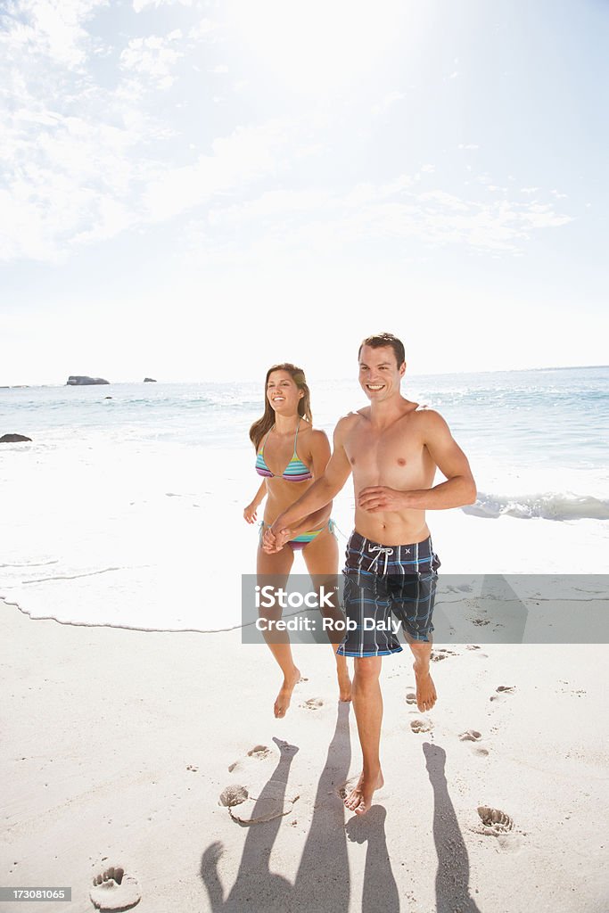 Souriant couple courir sur la plage, tenant les mains - Photo de 20-24 ans libre de droits