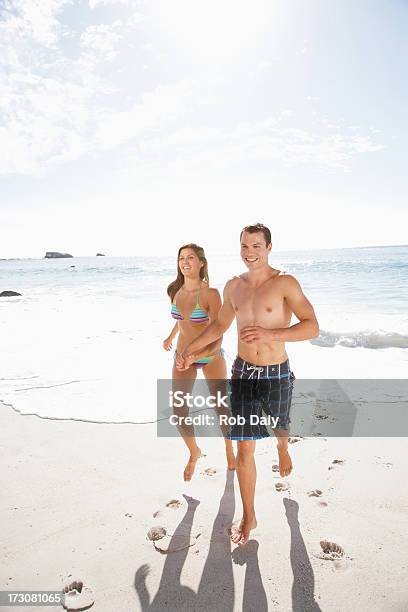 Photo libre de droit de Souriant Couple Courir Sur La Plage Tenant Les Mains banque d'images et plus d'images libres de droit de 20-24 ans