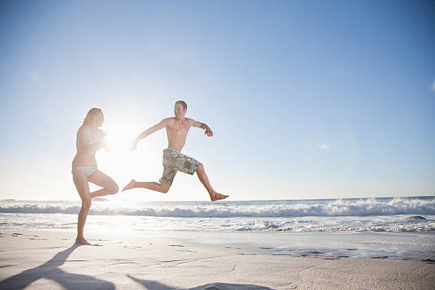 divertida pareja corriendo en la playa - swimming trunks bikini swimwear red fotografías e imágenes de stock