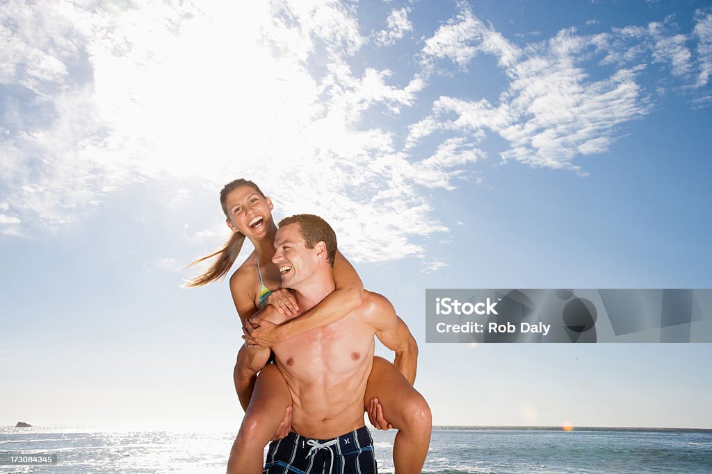 Joyeux homme donnant copine ride sur la plage Porter sur le dos - Photo de Mer libre de droits