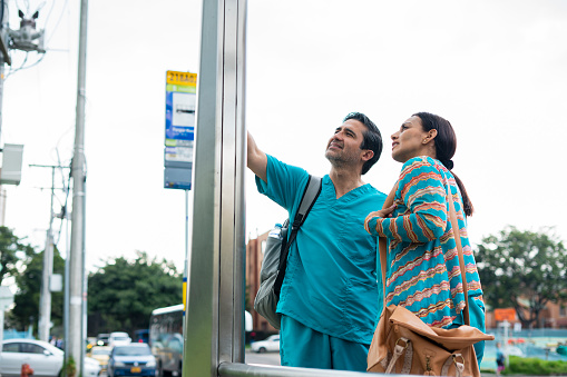 couple of adult doctors at bus stop, checking which route works for them at noon