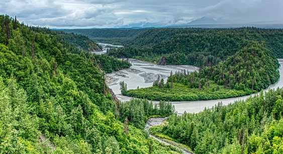 A scenic view of a river flowing through green mountains in Alaska