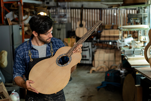 luthier carefully examines a piece of wood that will be used to make the neck of an acoustic guitar. The luthier is looking for the perfect piece of wood that will produce the desired sound.