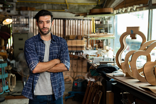 This portrait of a craftsman in his workshop features a young carpenter wearing a plaid shirt and apron. His happy demeanor and expertise shine through.