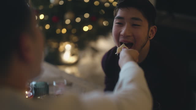 Asian Chinese gay person feeding partner in living room christmas party social gathering