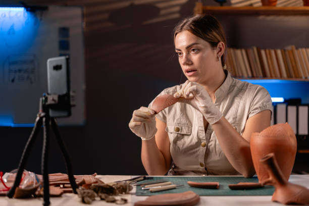 istock Female archaeologist doing research, uses smartphone to share discovery ancient civilization culture artifacts with followers in Internet. working late night in office 1730986022