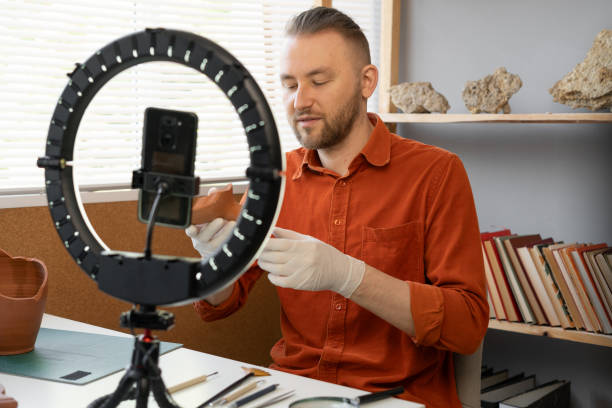 istock Archaeologist blogger broadcasts live with a ring lamp in his office working with ancient artifacts of prehistoric culture 1730986043
