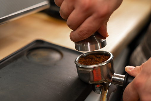 Barista holding portafilter and coffee tamper making an espresso in cafe, close-up. Copy space