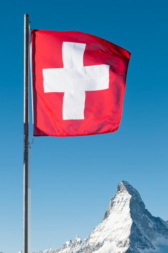 The Swiss flag flying in the wind, with the peak of the Matterhorn in the background.