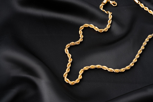 Gold chain on black silk fabric background close up