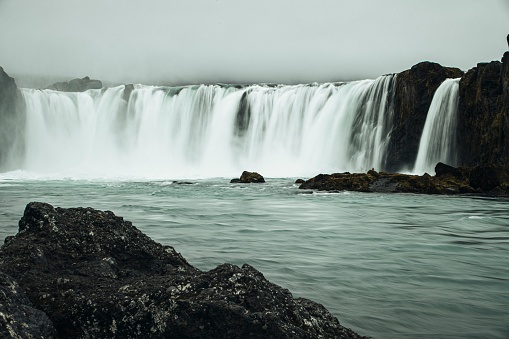 A majestic, crystal-clear waterfall cascading down a rocky cliff face in Godafoss, Iceland