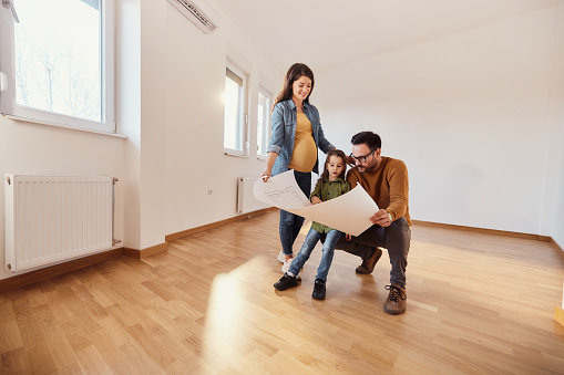 Young pregnant family examining blueprints after relocating into a new home. Copy space.