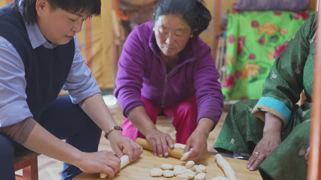 Asian Chinese female tourist learning preparing Mongolian traditional dumpling buuz with local Mongolian women in yurt kneading