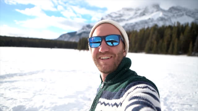 Young man taking selfie in winter near snowcapped mountains having fun in winter