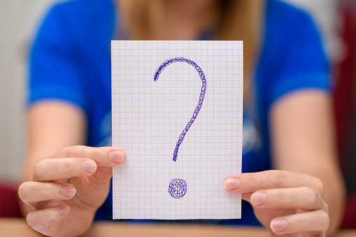 The woman is holding a piece of paper with a question mark drawn on it closeup