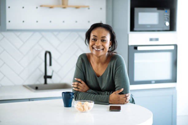 istock Casual African woman using phone in kitchen, looking at camera and smiling 1731114151