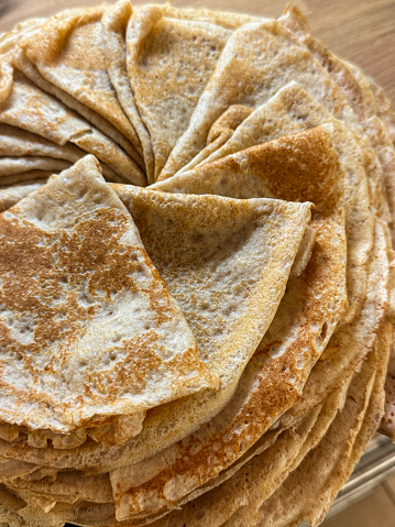 Stock photo showing a close-up, elevated view of a wood grain kitchen counter with a plate containing a spiral pile of freshly made French crepe pancakes which have been folded into quarters.