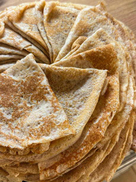 Close-up image of plate containing spiral stack of homemade, cooked French crepe pancake folded into quarters, wood grain kitchen counter, elevated view stock photo