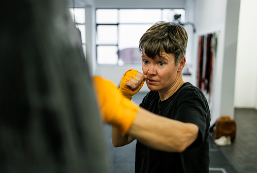 Mature female boxer hitting a punching bag during her training at a boxing gym