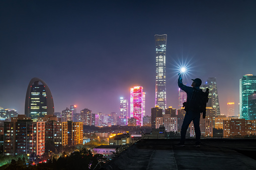 A photographer holding a light on the rooftop,The silhouette portrait at night in beijing cbd