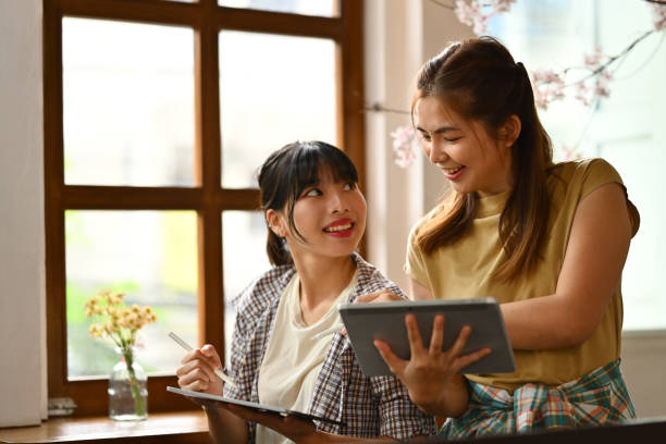 istock Smiling female designers holding digital tablet explaining details and sharing creative ideas to her colleague 1731184211