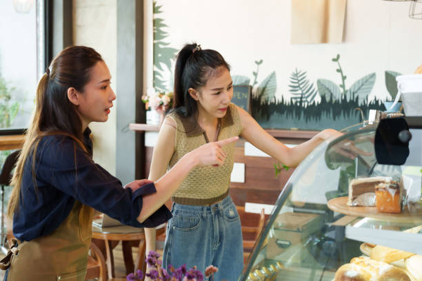 istock Asian coffee shop owner woman chatting with customer to order cake. Introducing different types of cakes in glass cabinets, male baristas chatting with customers ordering coffee drinks as well. 1731195568
