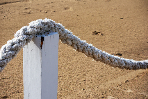A thick white rope in an arcuate shape hangs on wooden poles in the sea sand