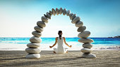 Young woman in yoga pose and stone bridge standing on the beach sands. Welness and spirituality concept