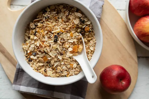 Delicious and healthy homemade muesli or granola with rolled oats, puffed amaranth and quinoa and dried fruits. Served in a large bowl with spoon on light wooden background. Closeup
