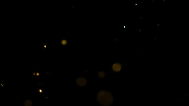 gold glow particles bokeh sparkle glittering on black background, holiday christmas new year celebration