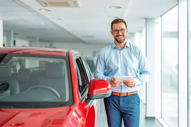 Cheerful sales manager with tablet computer standing near new automobile at luxury car salon, copy space stock photo