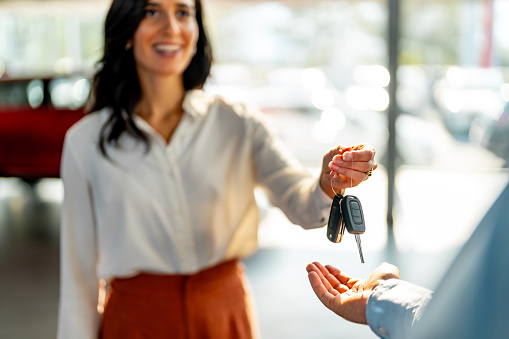 Smiling woman is giving car key to a male customer.